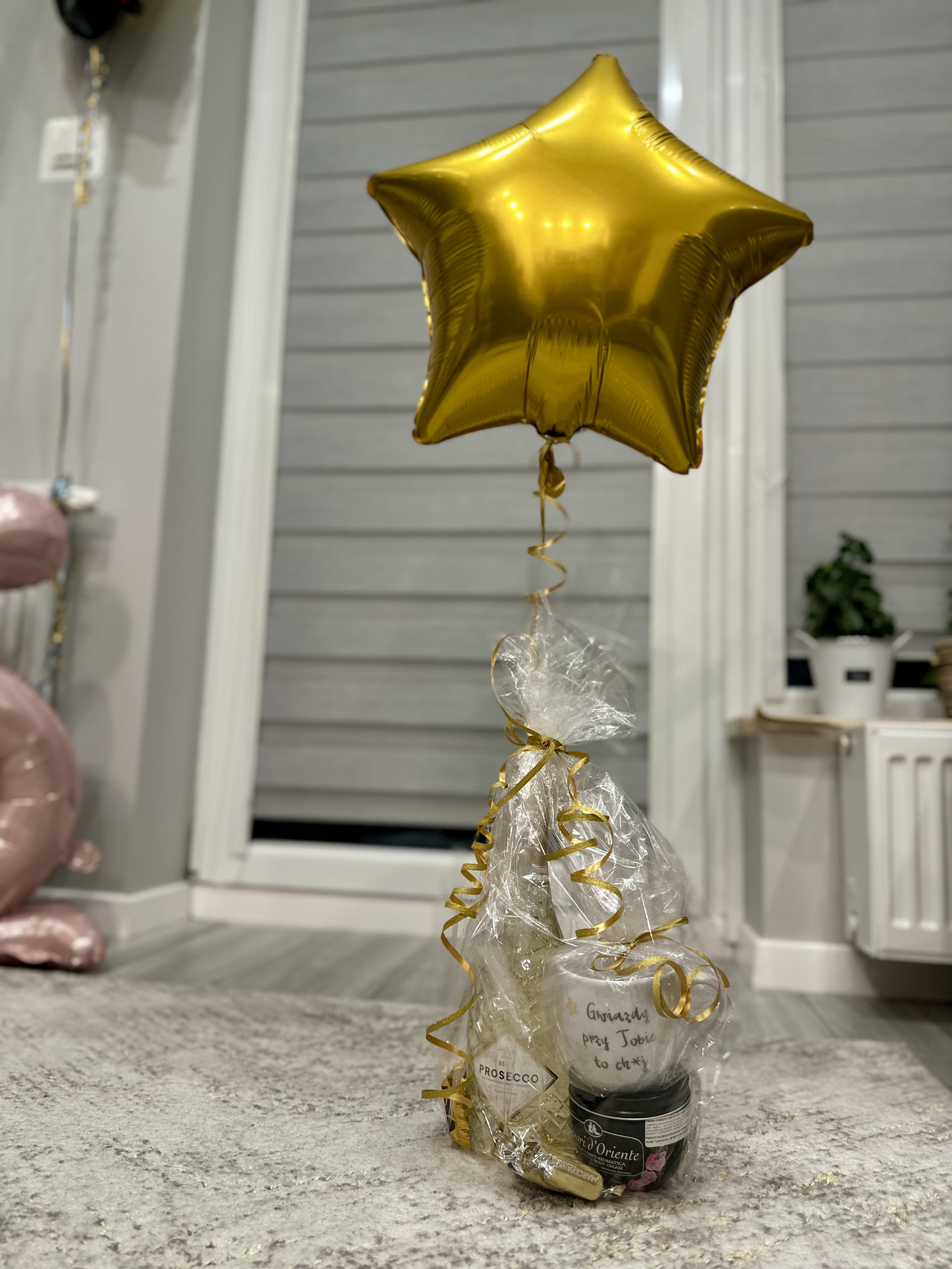 Prezent owinięty celofanem przywiązany balon napompowany helem w kształcie złotej gwiazdy