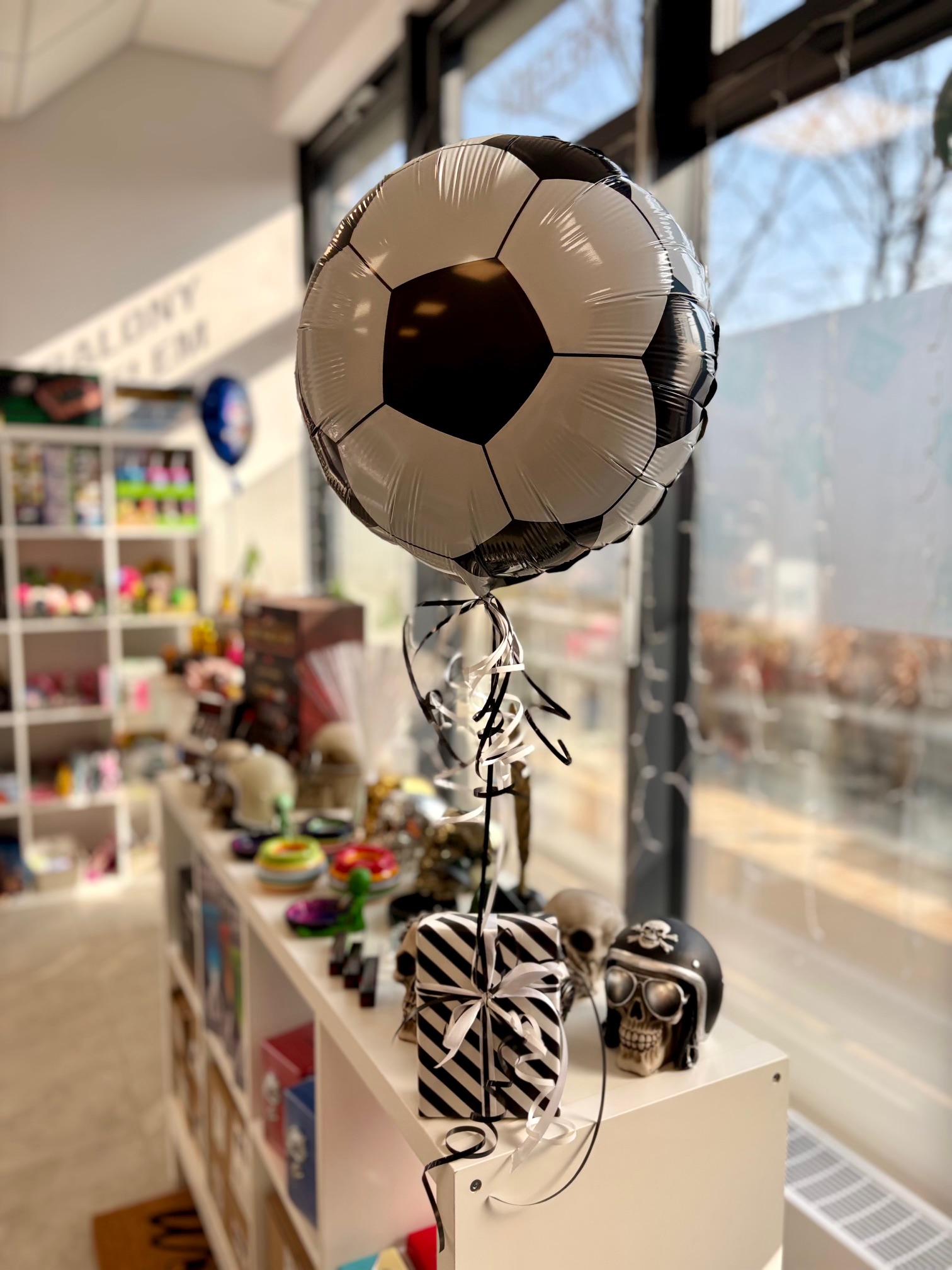 Prezent dla kibica, fana piłki nożnej, lampka zapakowana w czarno-biały papier ozdobny, do którego przywiązany jest balon helowy w kształcie piłki nożnej